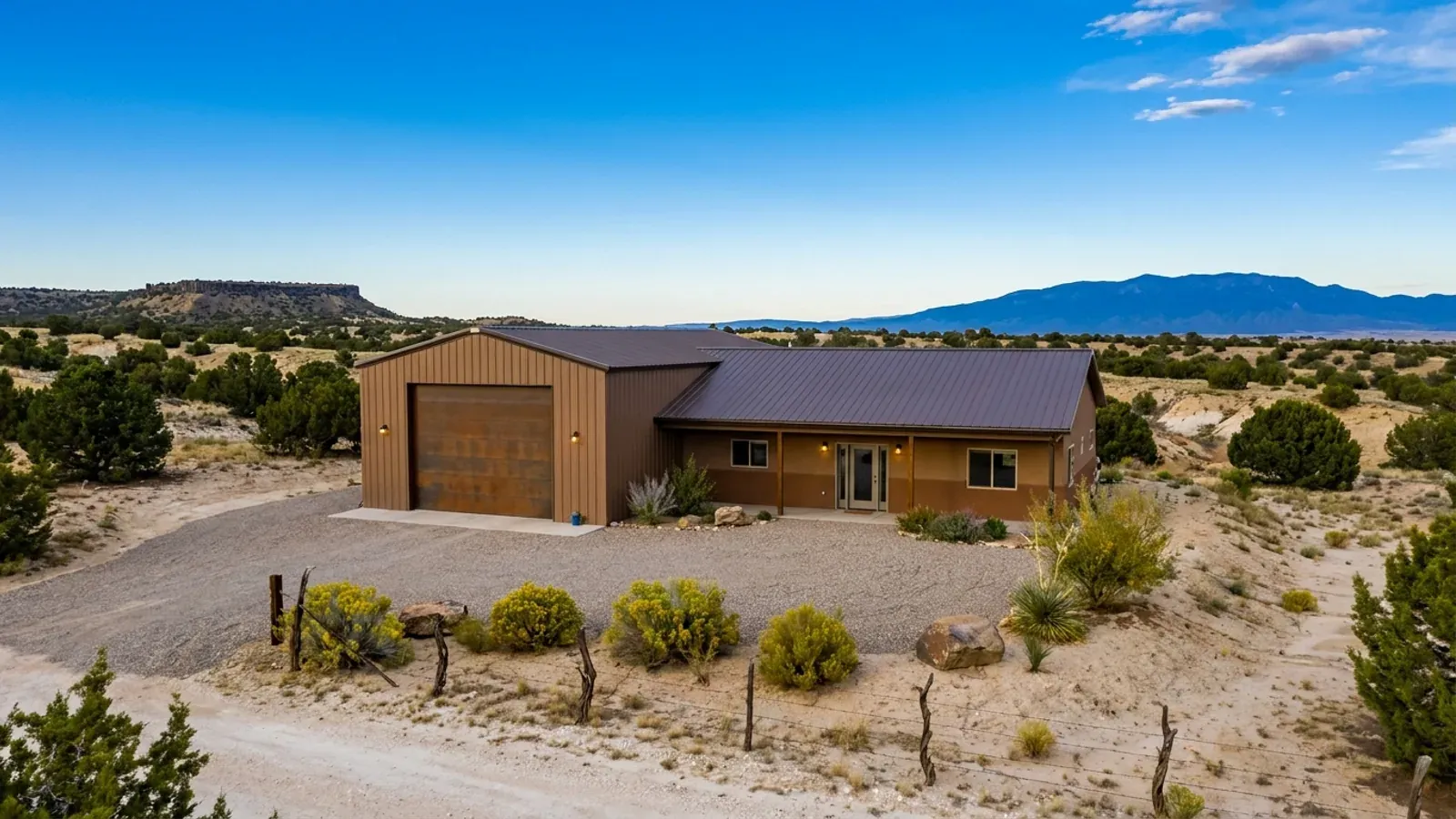 A barndominium with a tall, deep RV garage bay attached to the residence under one continuous roof, in open high desert.